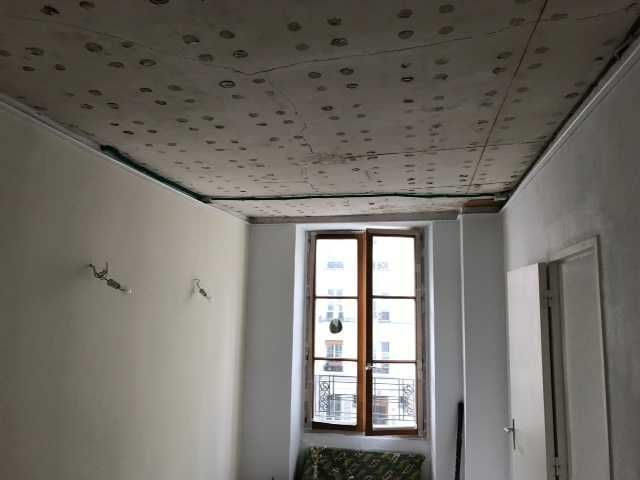 Pièce blanche vide en cours de rénovation, avec fenêtre et plafond à motifs