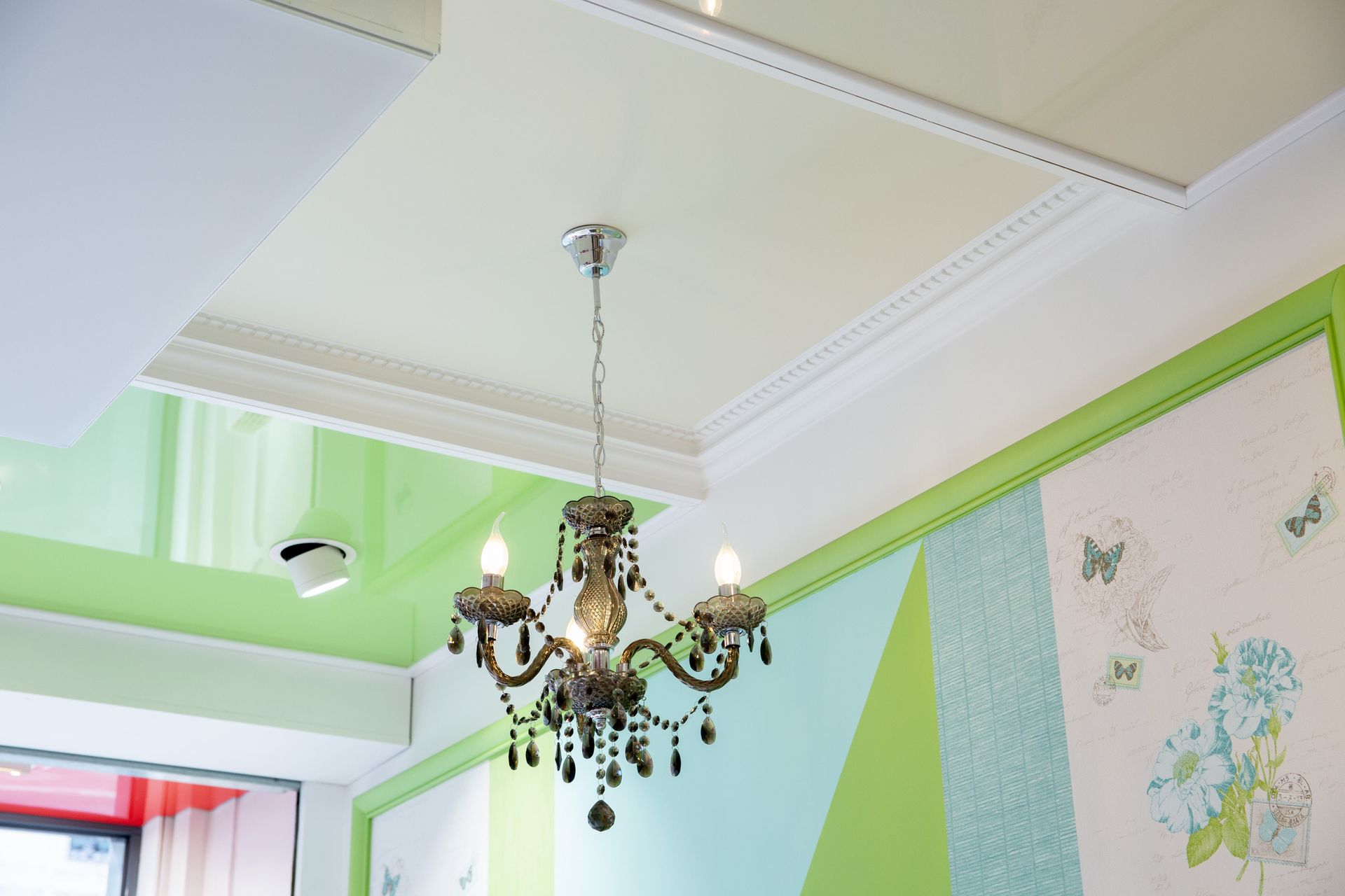 Un lustre orné suspendu à un plafond vert pâle et blanc dans une pièce lumineuse