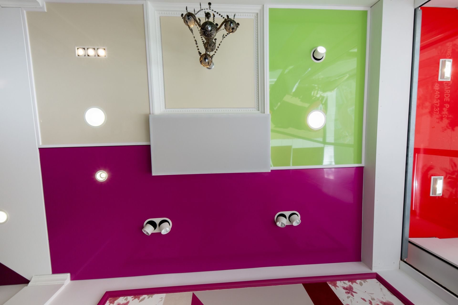 Mur de salle de bain coloré avec des panneaux magenta et verts, lavabo, lumières et lustre.
