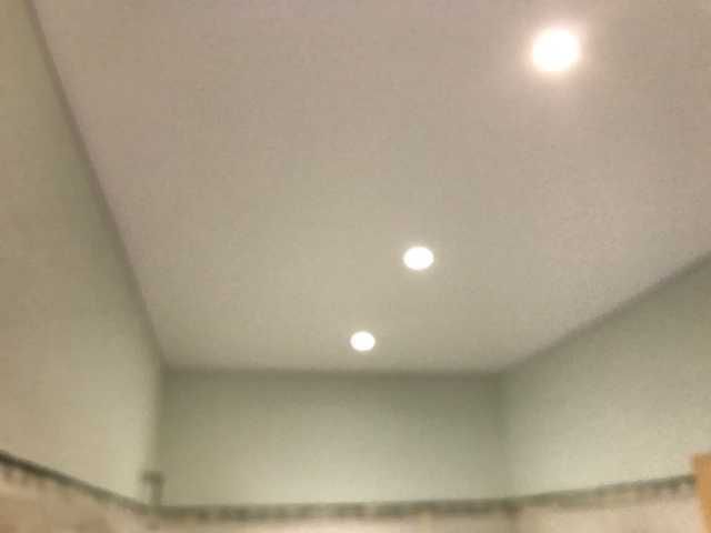Plafond blanc avec spots encastrés au-dessus de murs vert pâle et de moulures carrelées dans un coin de la pièce