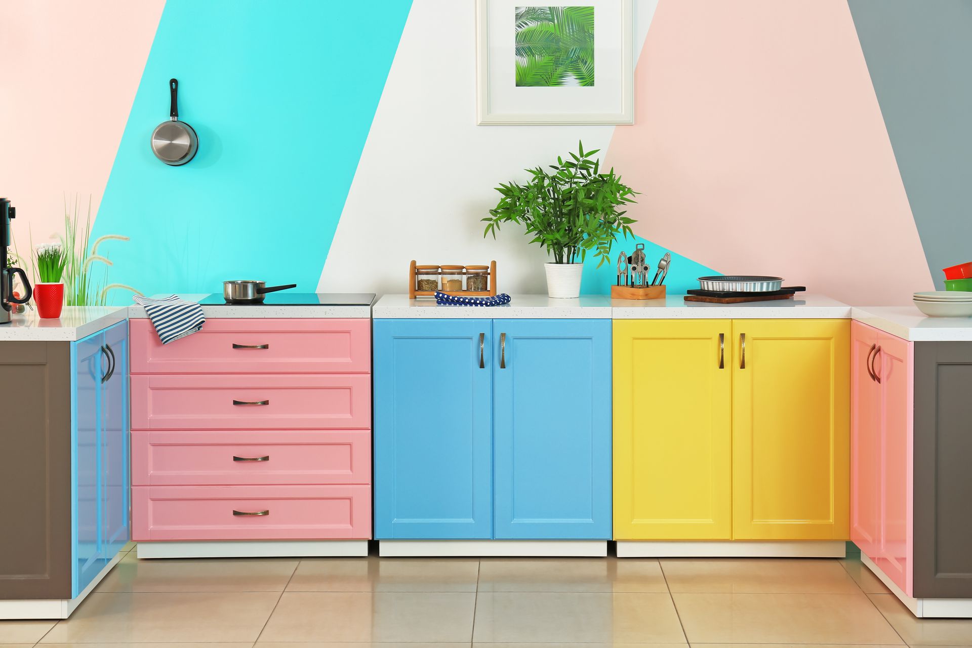 Cuisine colorée avec des placards rose pastel, bleus et jaunes et un mur bleu sarcelle clair