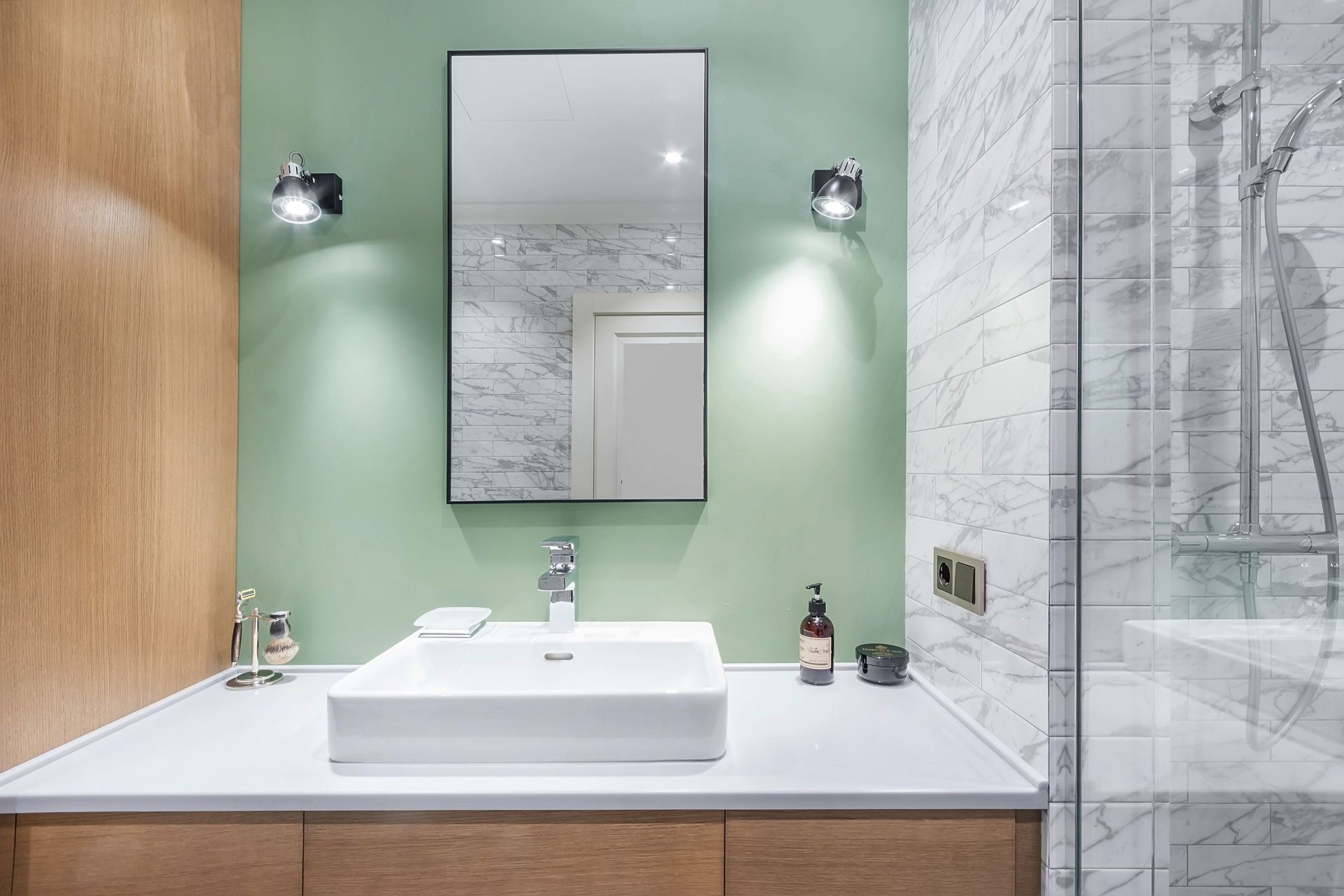Salle de bains moderne avec murs verts, meuble-lavabo en bois, lavabo blanc, miroir et cabine de douche en verre