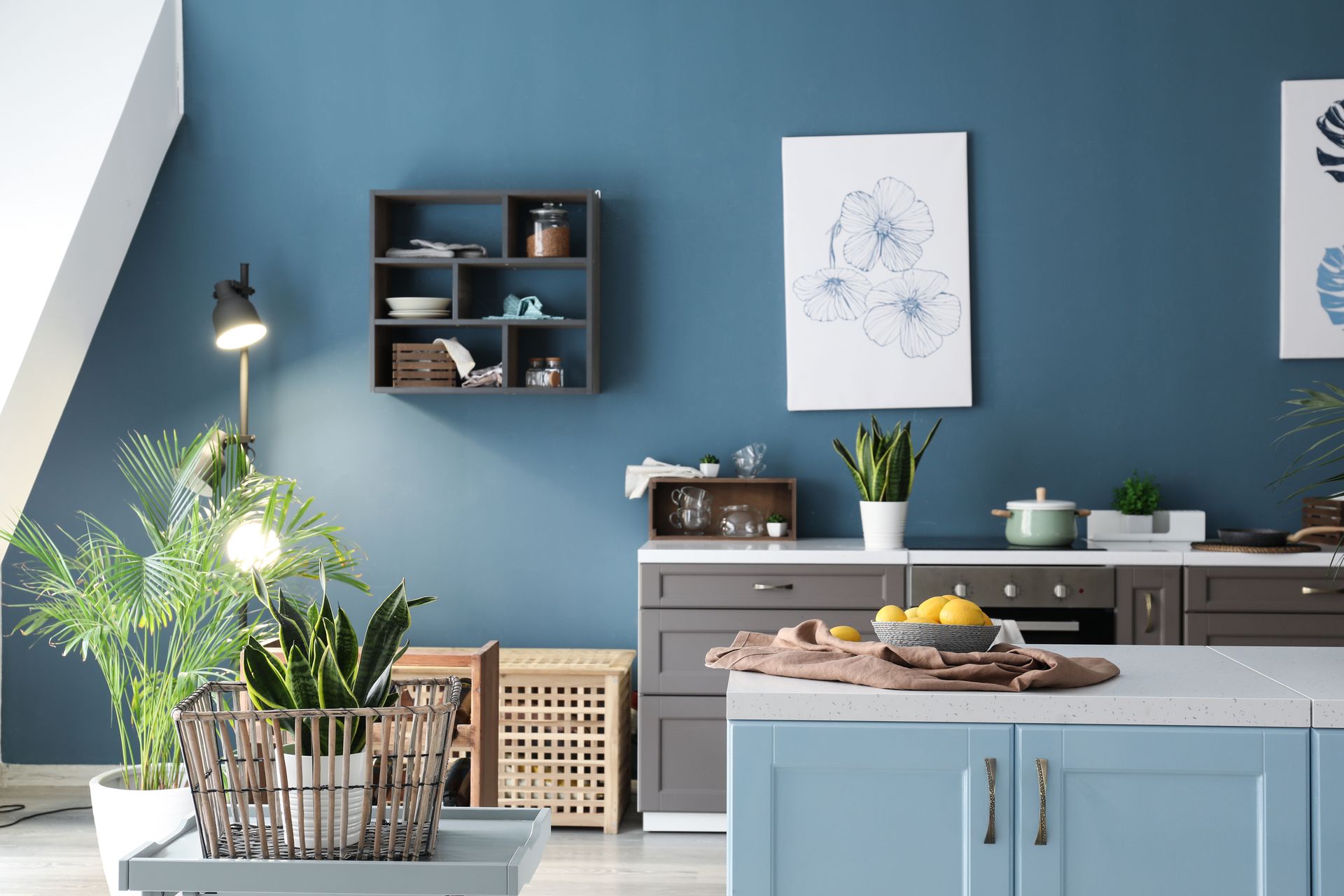 Cuisine moderne avec murs bleus, plantes, étagères ouvertes et îlot gris avec fruits et ustensiles de cuisine.