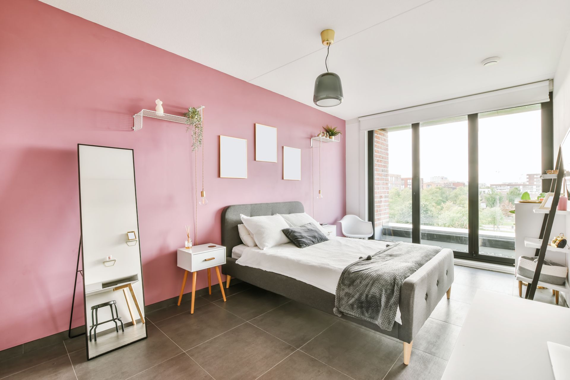 Chambre rose vif avec un lit, des miroirs, un bureau et de grandes fenêtres donnant sur les arbres