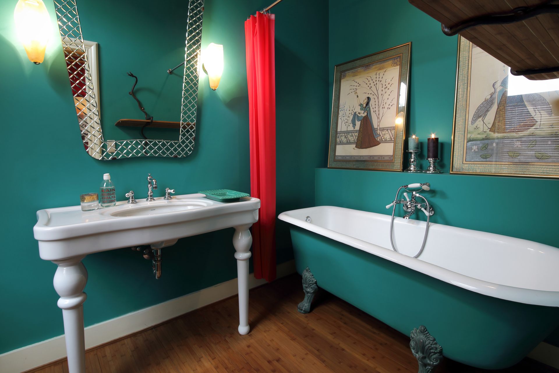 Salle de bains turquoise avec lavabo sur pied, baignoire sur pattes, rideau rouge et appliques murales.