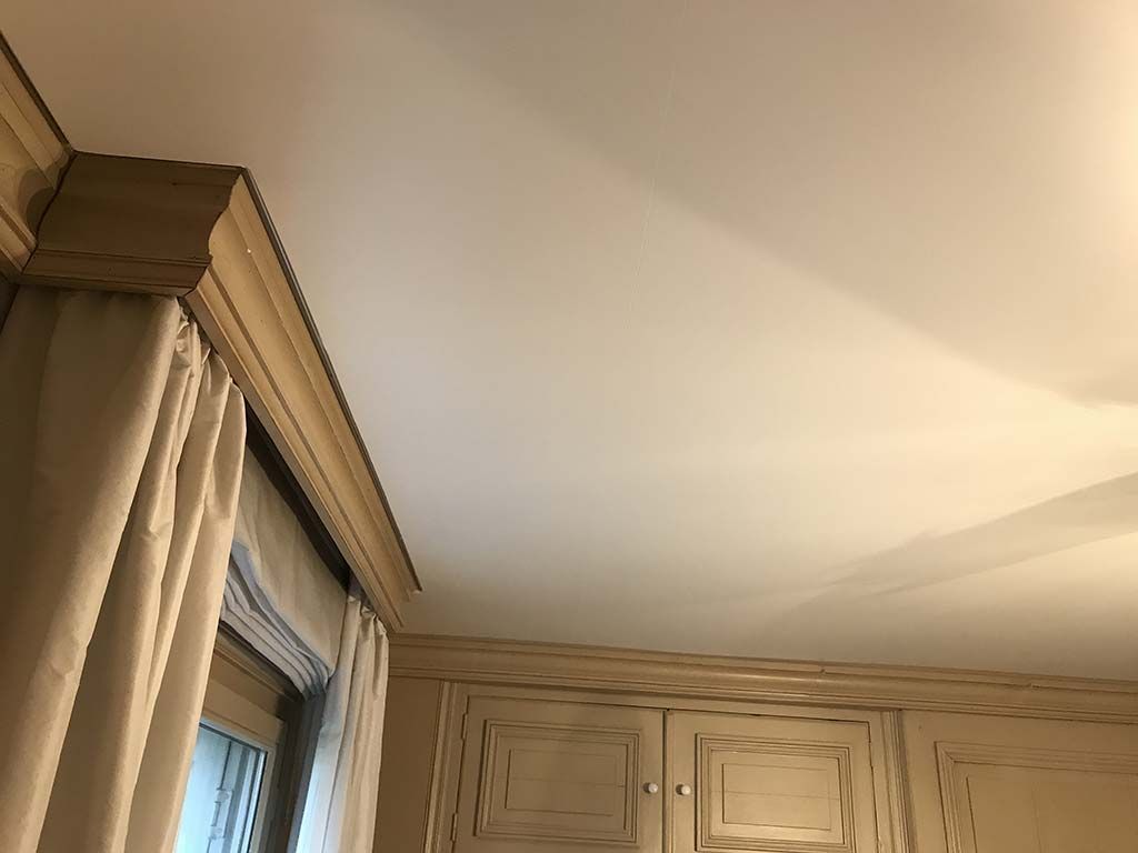 Coin d'une pièce avec des placards couleur crème, un rideau et une fenêtre sous une douce lumière de plafond