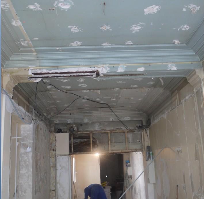 Scène de rénovation : plafond et murs inachevés du couloir, avec plâtre irrégulier et câbles électriques apparents.