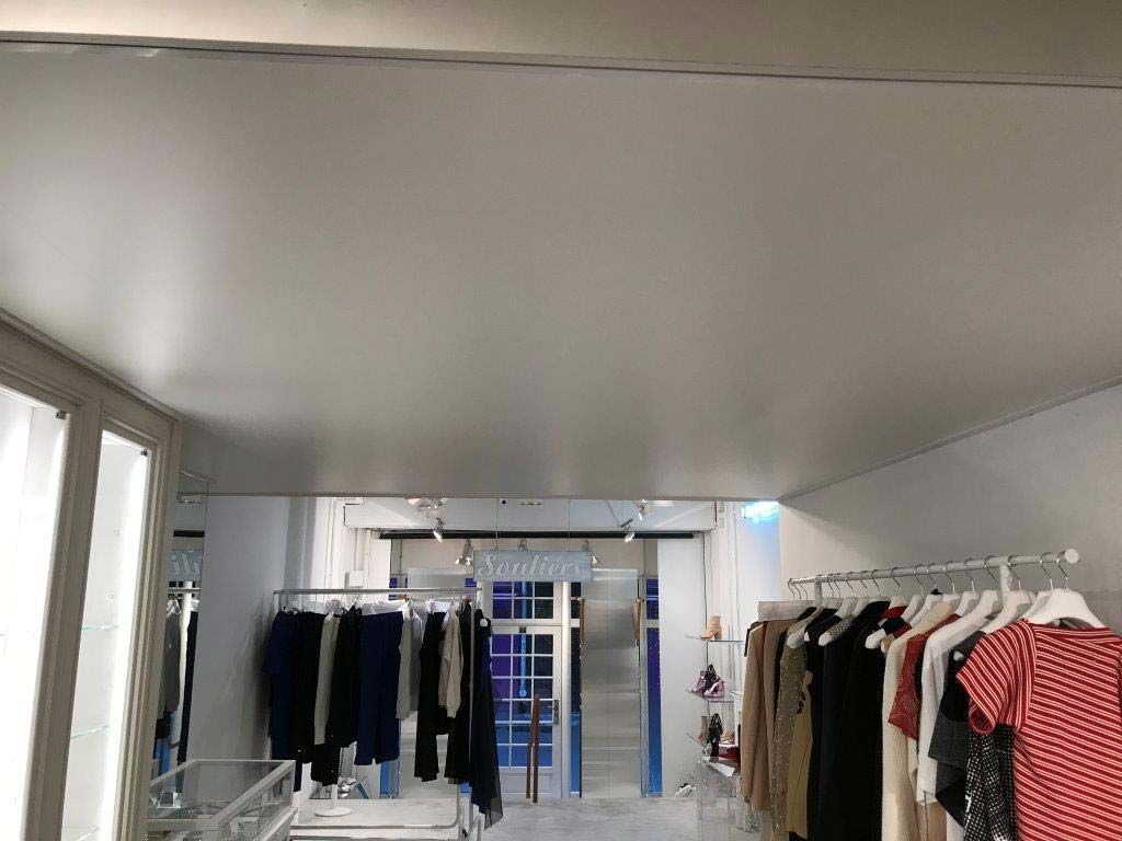Des portants à vêtements dans un magasin lumineux aux murs blancs et au plafond mansardé.