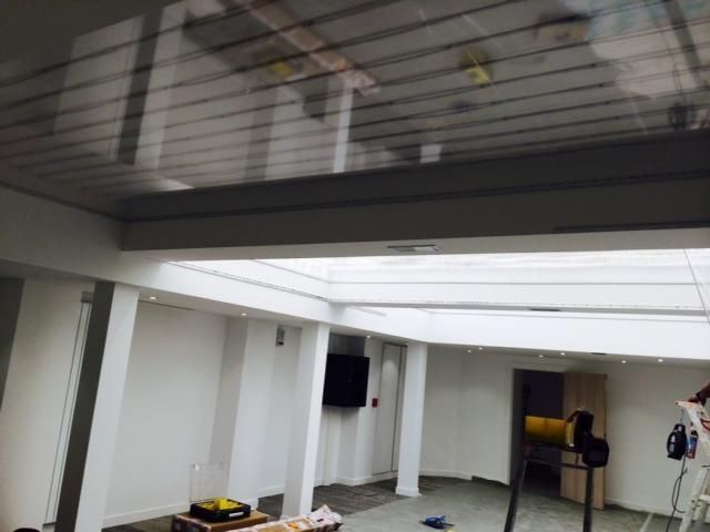 Pièce intérieure vide aux murs blancs, au plafond apparent, et une personne debout près d'une table au fond.