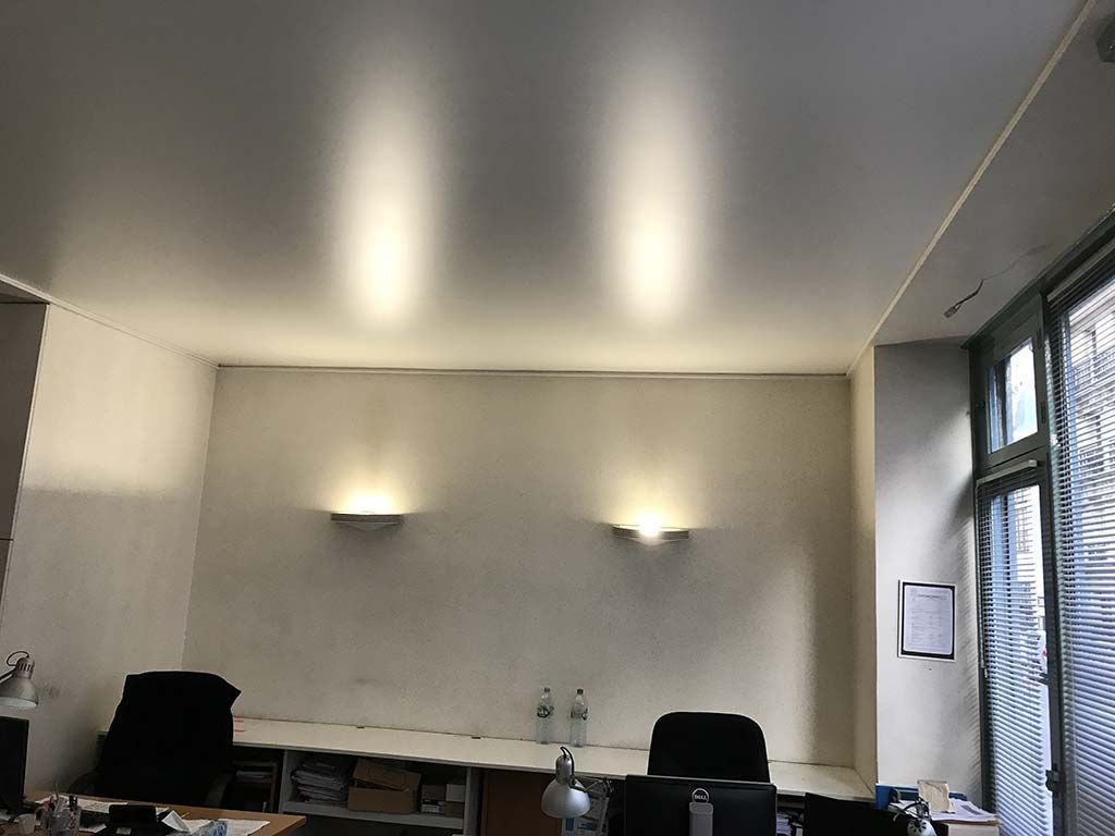 Intérieur d'un petit bureau avec bureaux, chaises, appliques murales et une fenêtre sur la droite.