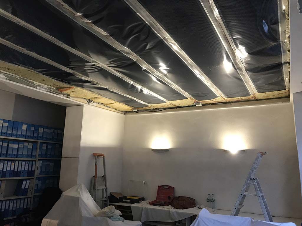 Pièce inachevée avec poutres apparentes au plafond, appliques murales, échelle et matériaux empilés au sol