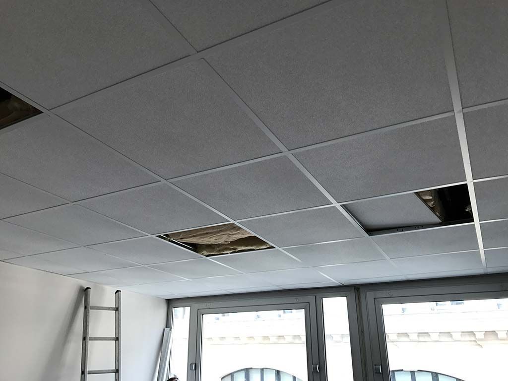 Plafond de bureau endommagé avec des interstices, une échelle et des fenêtres en dessous