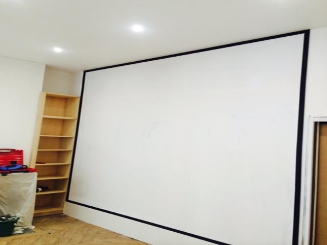 Pièce vide avec un grand écran de projection blanc au mur et une étagère en bois dans un coin.