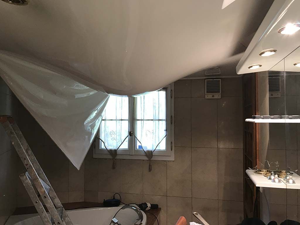 Pièce intérieure avec une bâche blanche affaissée sous le plafond, une fenêtre, une échelle et un mur carrelé.