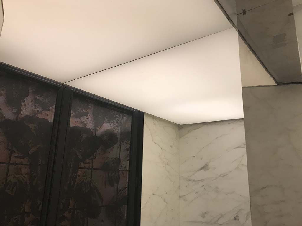 Plafond intérieur moderne avec éclairage blanc doux et murs à motifs marbrés jouxtant une cloison sombre