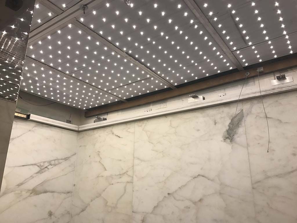 Intérieur d'ascenseur moderne avec murs en marbre et plafond illuminé.