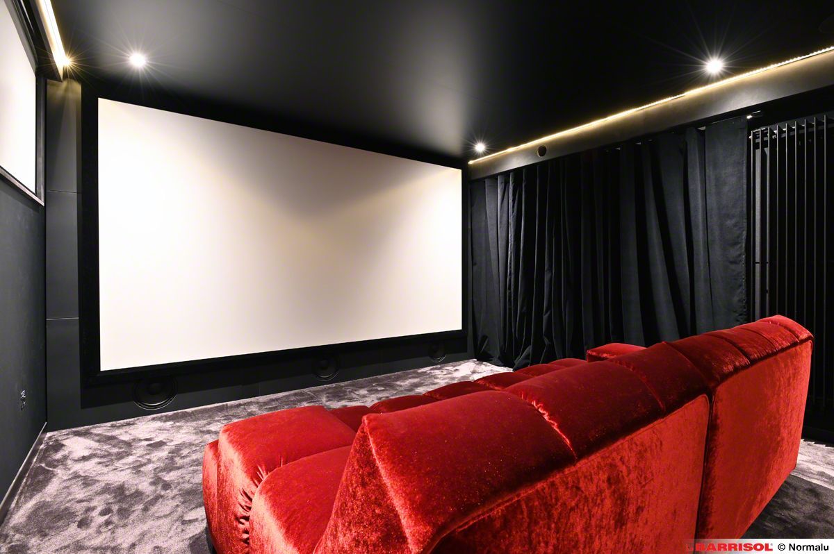 Salle de cinéma maison avec un grand écran blanc, des fauteuils inclinables rouges, des murs noirs.