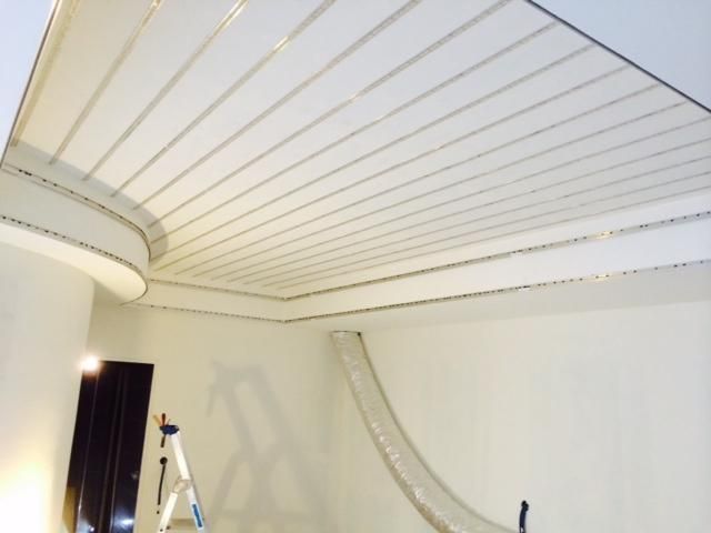 Plafond blanc orné de longues moulures parallèles dans une pièce en rénovation, avec une échelle en dessous.