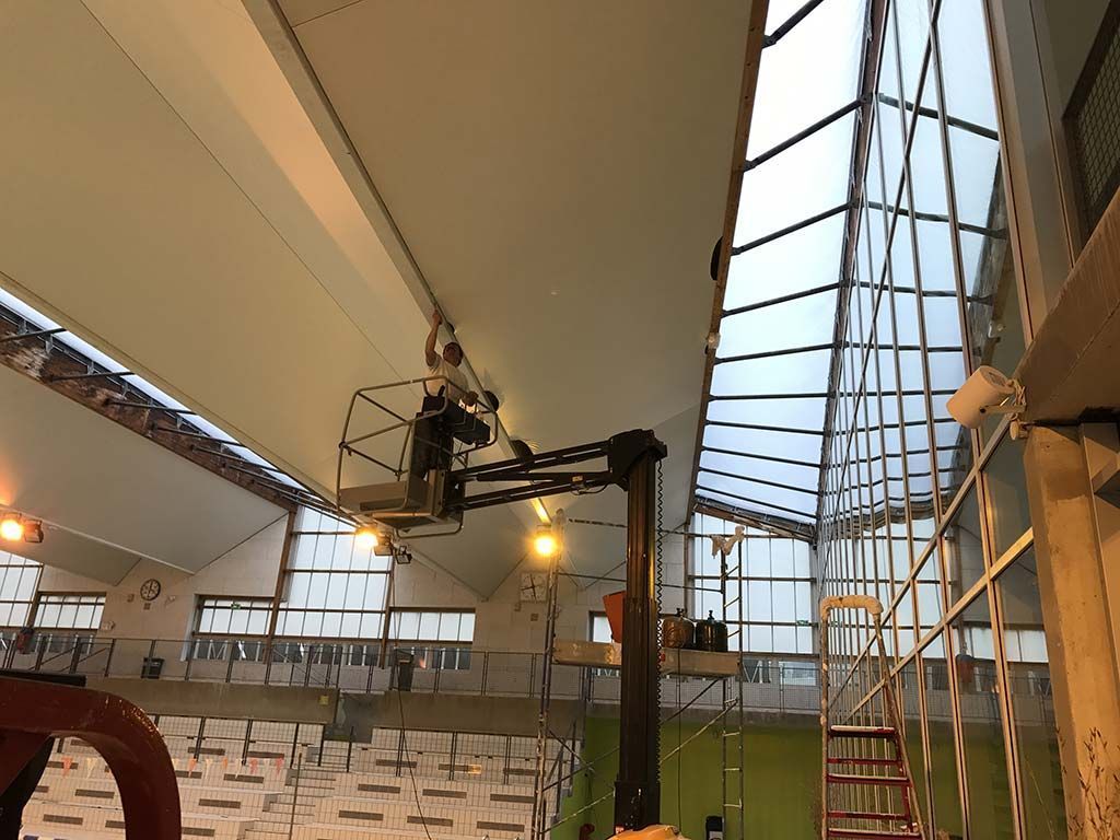 Arène intérieure avec une grue de caméra, des rangées de sièges et une échelle rouge sous un haut toit de verre