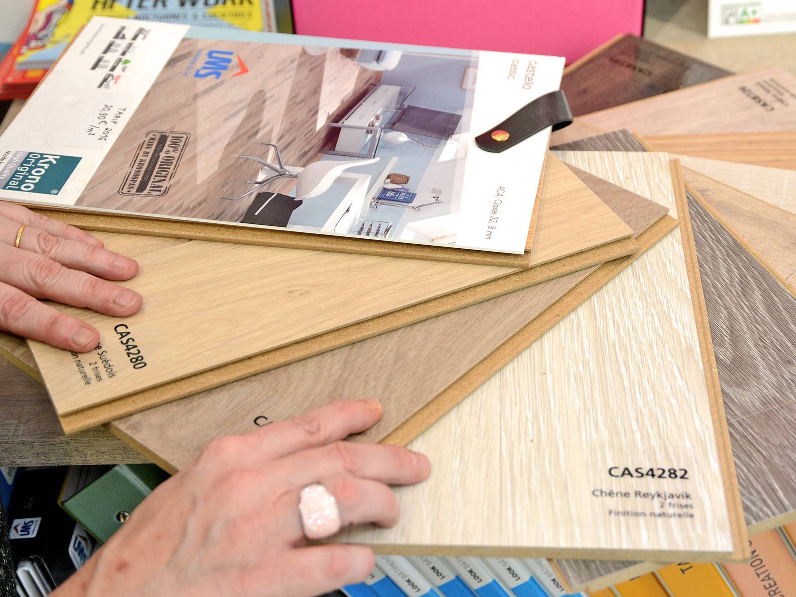 Des mains tenant plusieurs échantillons de parquet avec une brochure posée dessus.