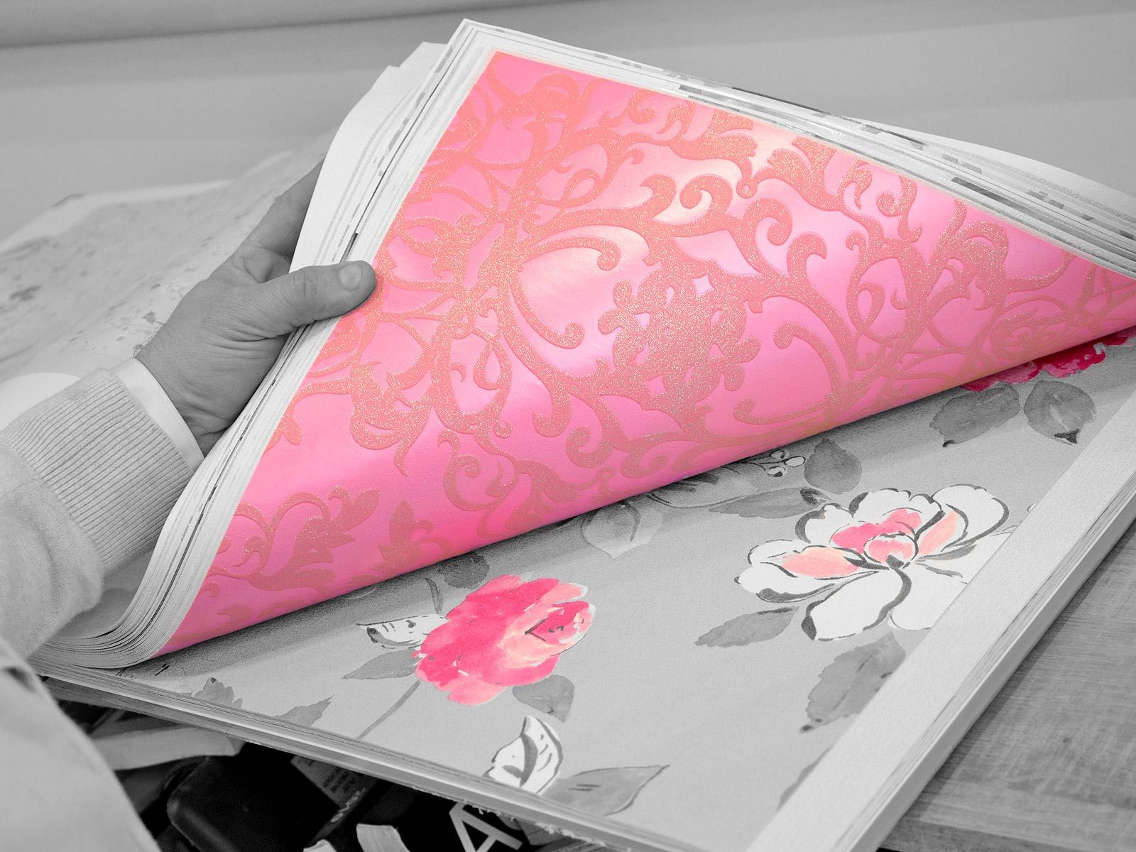 Une main tourne une page pour révéler le dessous rose à motifs d'un livre en tissu fleuri