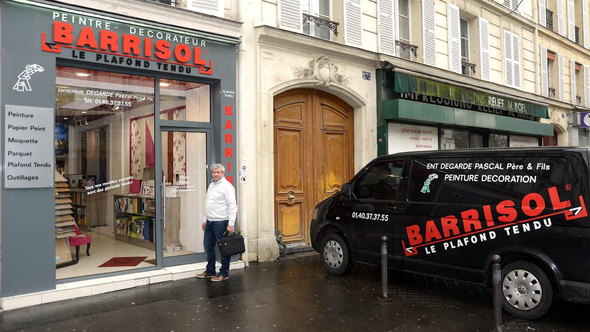 Façade du magasin BARRISOL dans une rue pluvieuse, une camionnette noire garée devant et une personne près de la porte.