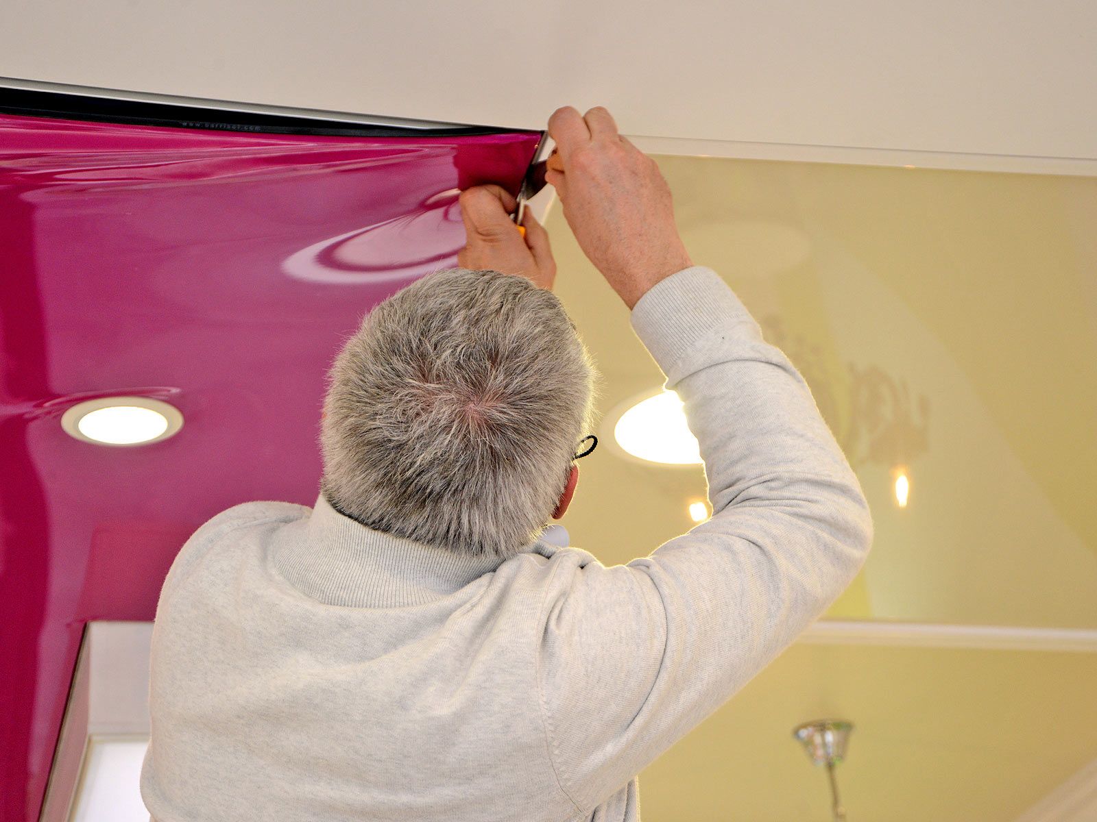 Un homme suspend un panneau magenta à un rail de plafond dans une pièce éclairée par des spots encastrés.