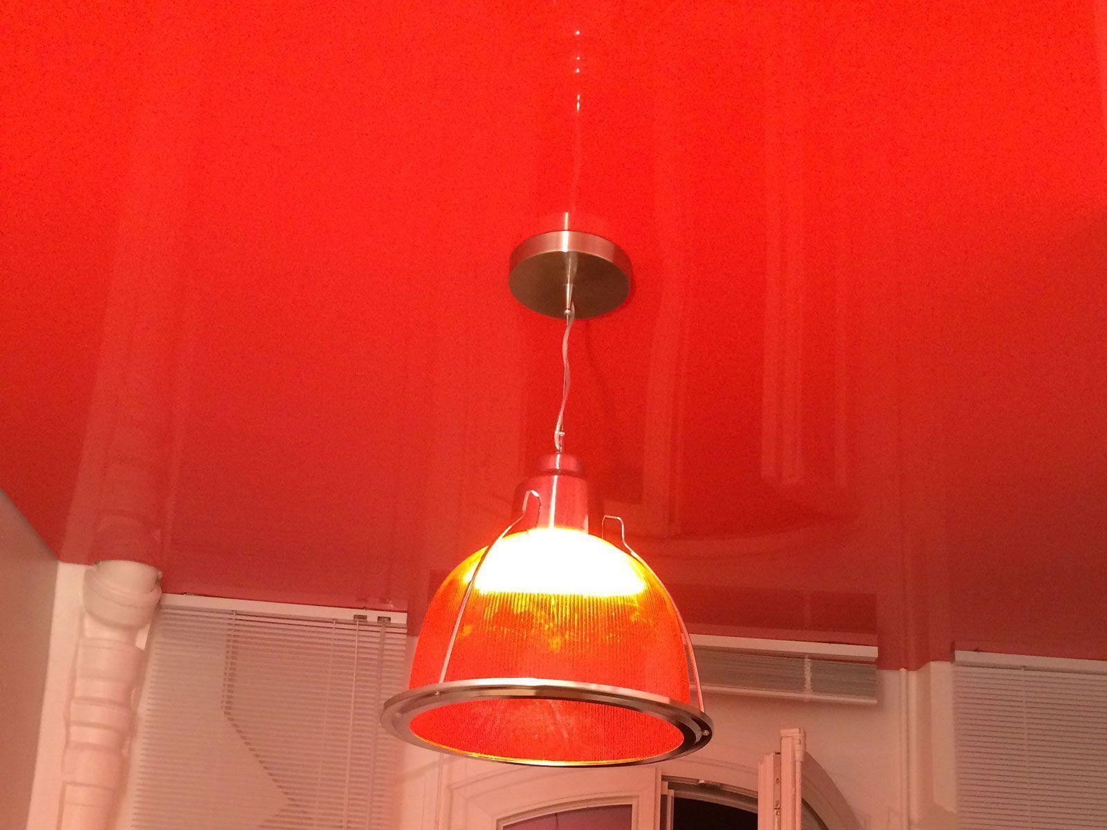 Une suspension rouge illumine un plafond rouge, avec un mur de briques blanches en arrière-plan.