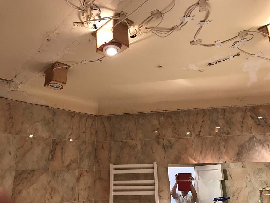 Salle de bains avec murs en marbre, câblage apparent au plafond, un luminaire et une échelle blanche près d'une porte.