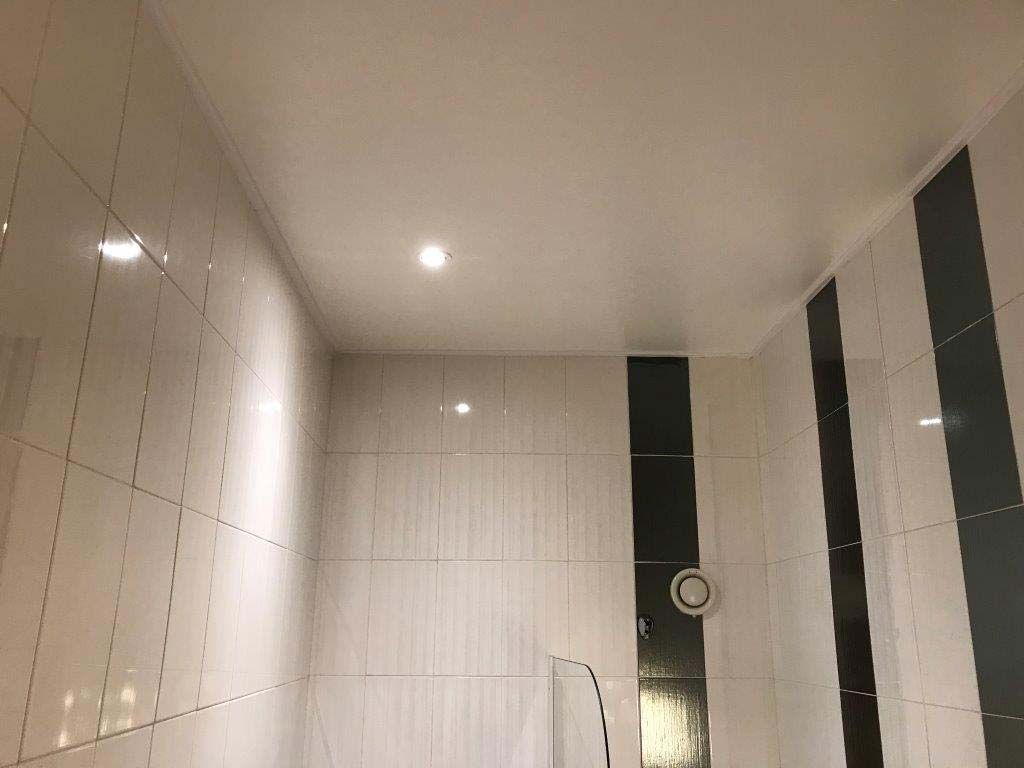 Salle de bains carrelée de blanc avec éclairage encastré au plafond et carreaux noirs décoratifs au mur.