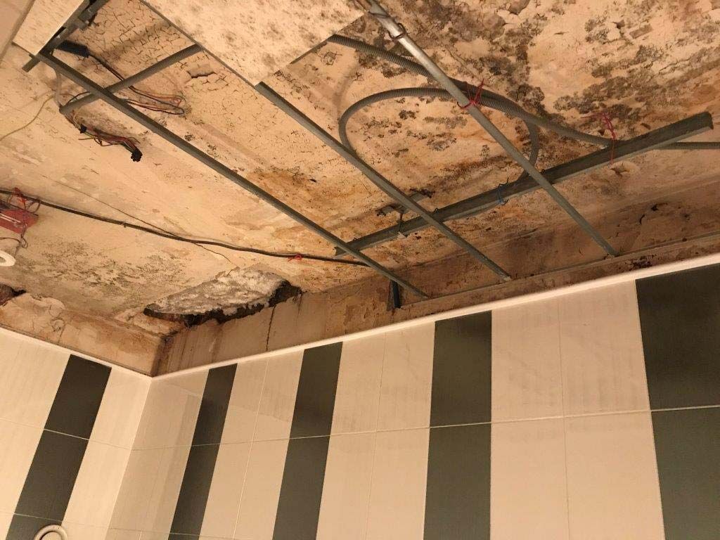 Plafond endommagé avec ossature métallique apparente et plâtre qui s'écaille au-dessus de panneaux muraux rayés
