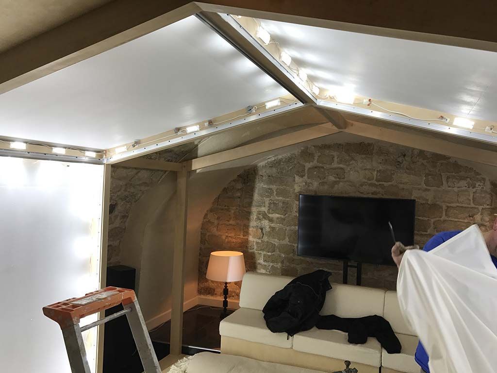 Salon mansardé confortable avec murs de briques apparentes, canapé, télévision, lampe et fauteuil drapé blanc