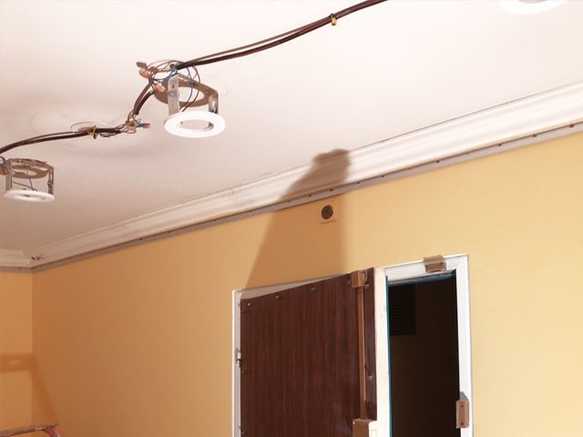 Rail d'éclairage et câblage au plafond au-dessus d'un mur beige avec une porte ouverte