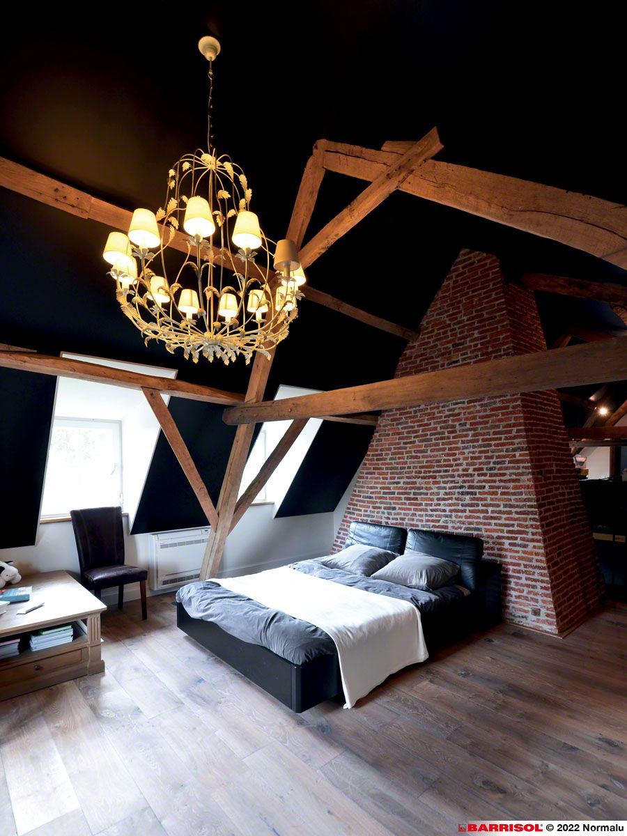 Chambre rustique avec poutres apparentes, cheminée en briques, lustre et lit avec literie foncée