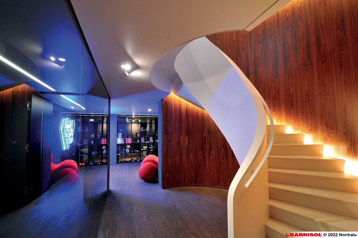 Intérieur moderne avec escalier blanc incurvé, mur lambrissé et coin salon éclairé de bleu
