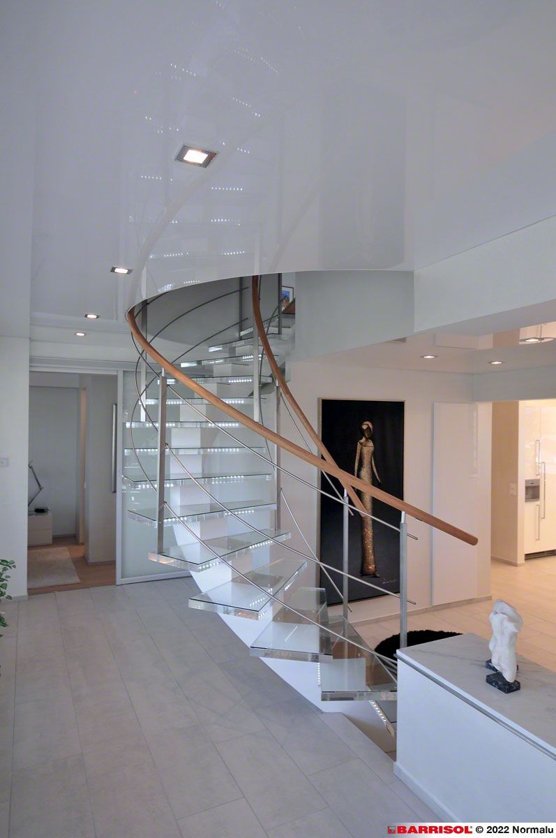 Escalier en verre courbé dans un showroom moderne à l'intérieur blanc, avec un mannequin à proximité.
