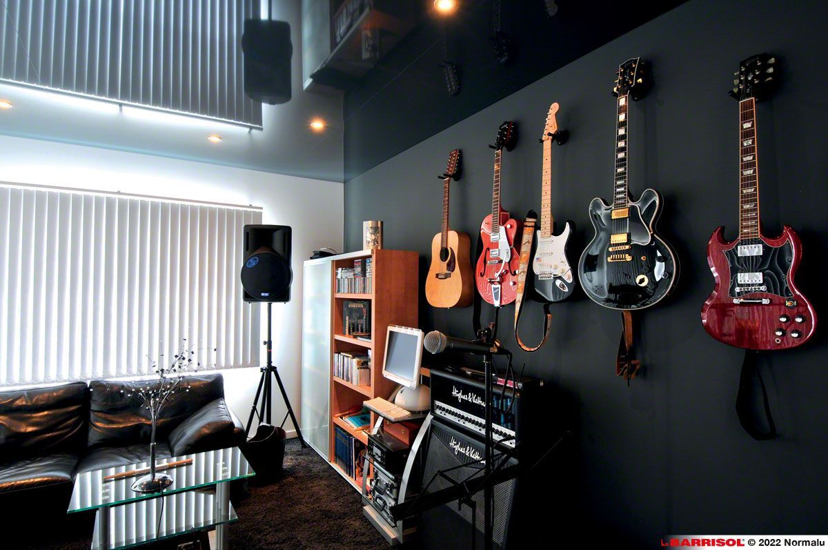 Studio de musique moderne avec des guitares accrochées à un mur noir, un canapé, des enceintes et un petit coin bureau.
