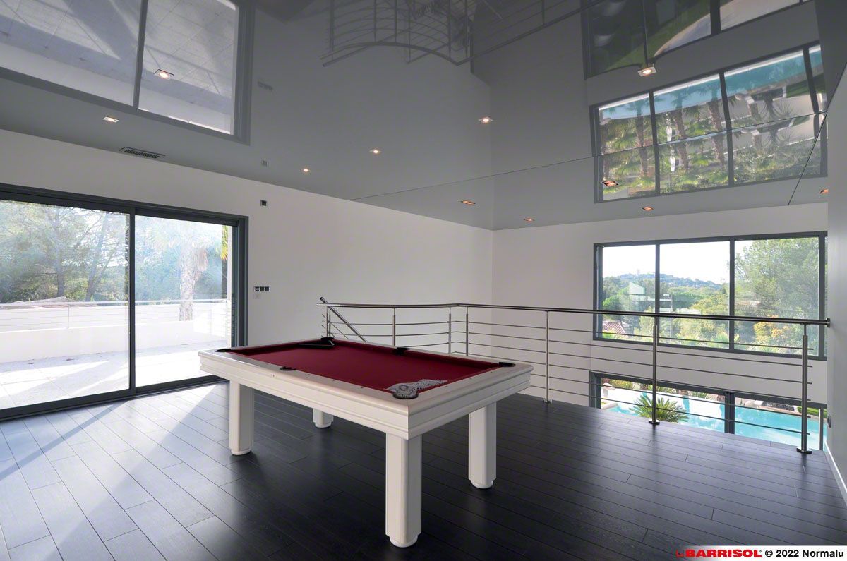 Salon moderne avec table de billard, baies vitrées et lumière naturelle abondante