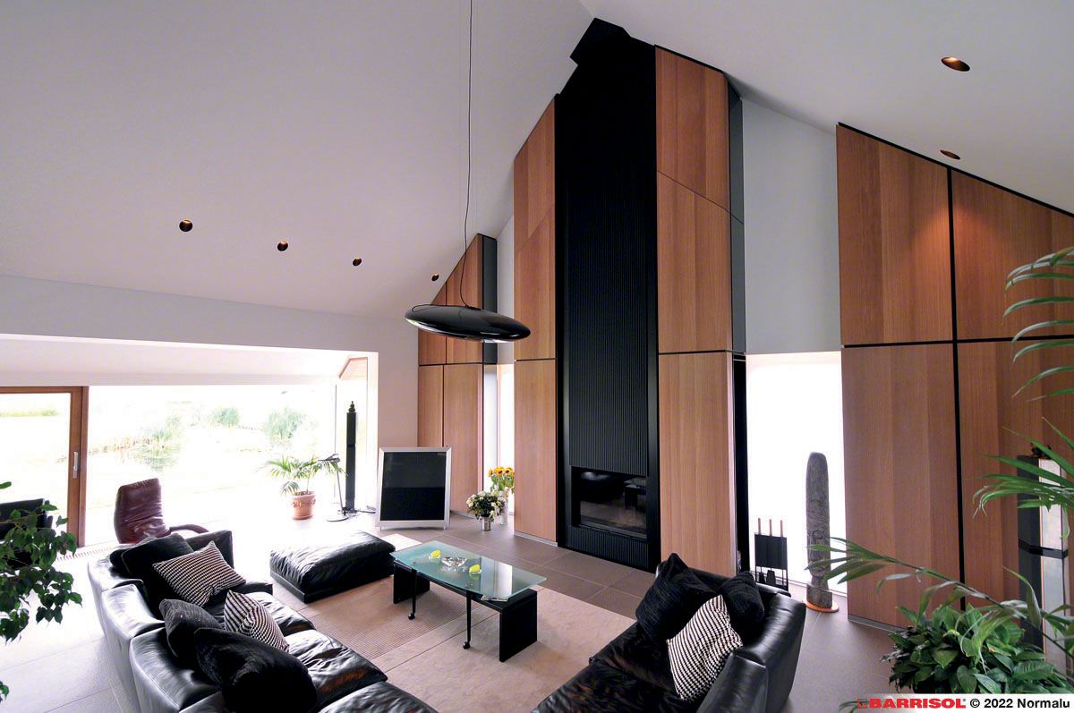 Salon moderne avec fauteuils en cuir noir, hautes boiseries, cheminée et fenêtres allant du sol au plafond