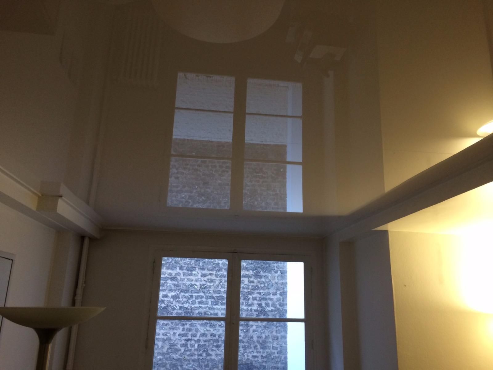Salon avec haut plafond, de grandes fenêtres et la lumière du soleil se reflétant sur le plafond.