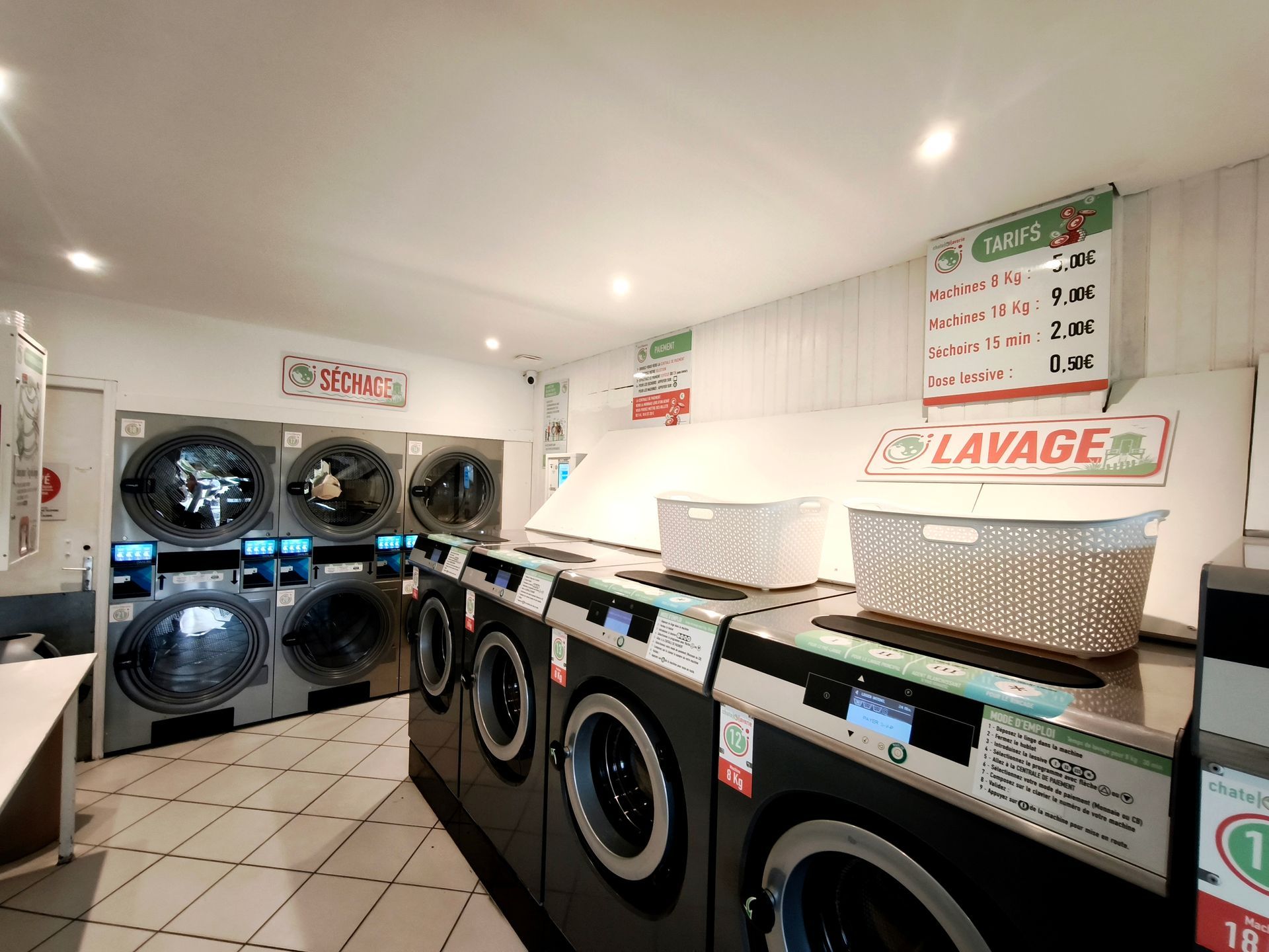 Laverie avec des rangées de lave-linge et de sèche-linge à hublot sous un éclairage vif au plafond.