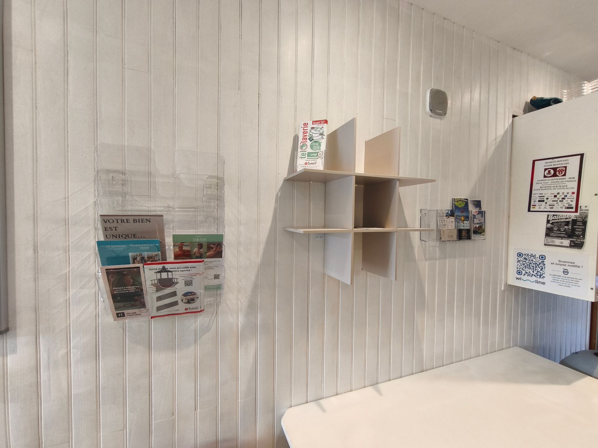 Pièce blanche lambrissée avec des étagères murales, des magazines et une banquette pour s'asseoir.