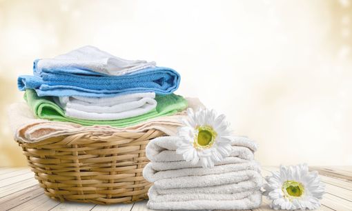 Panier en osier avec des serviettes pliées empilées et des marguerites blanches.