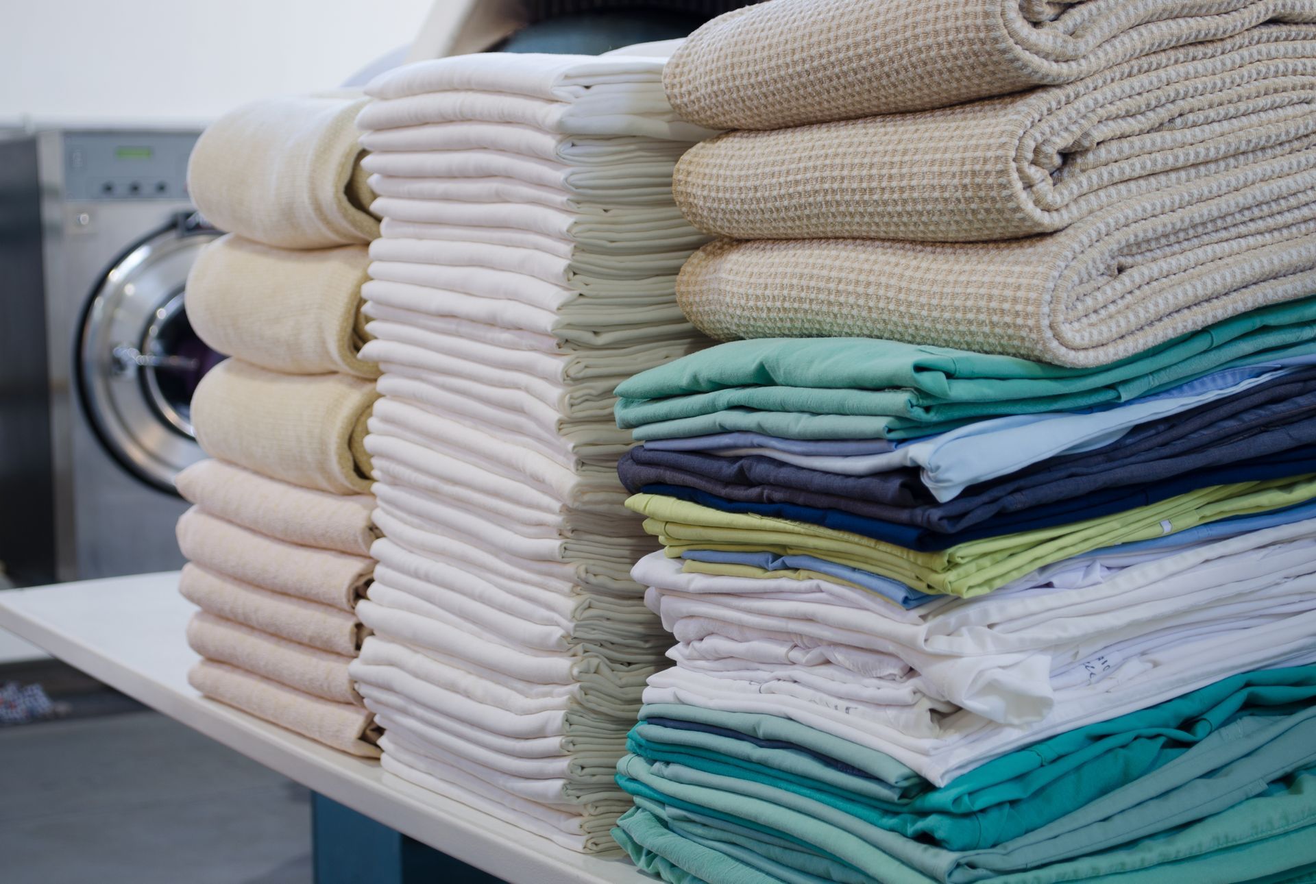 Des serviettes et du linge soigneusement pliés, empilés sur une table de buanderie à côté d’une machine à laver.
