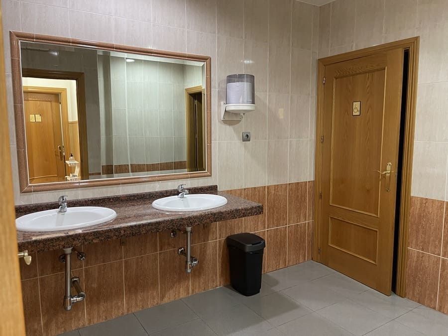 Un baño con dos lavabos, un espejo y un cubo de basura.