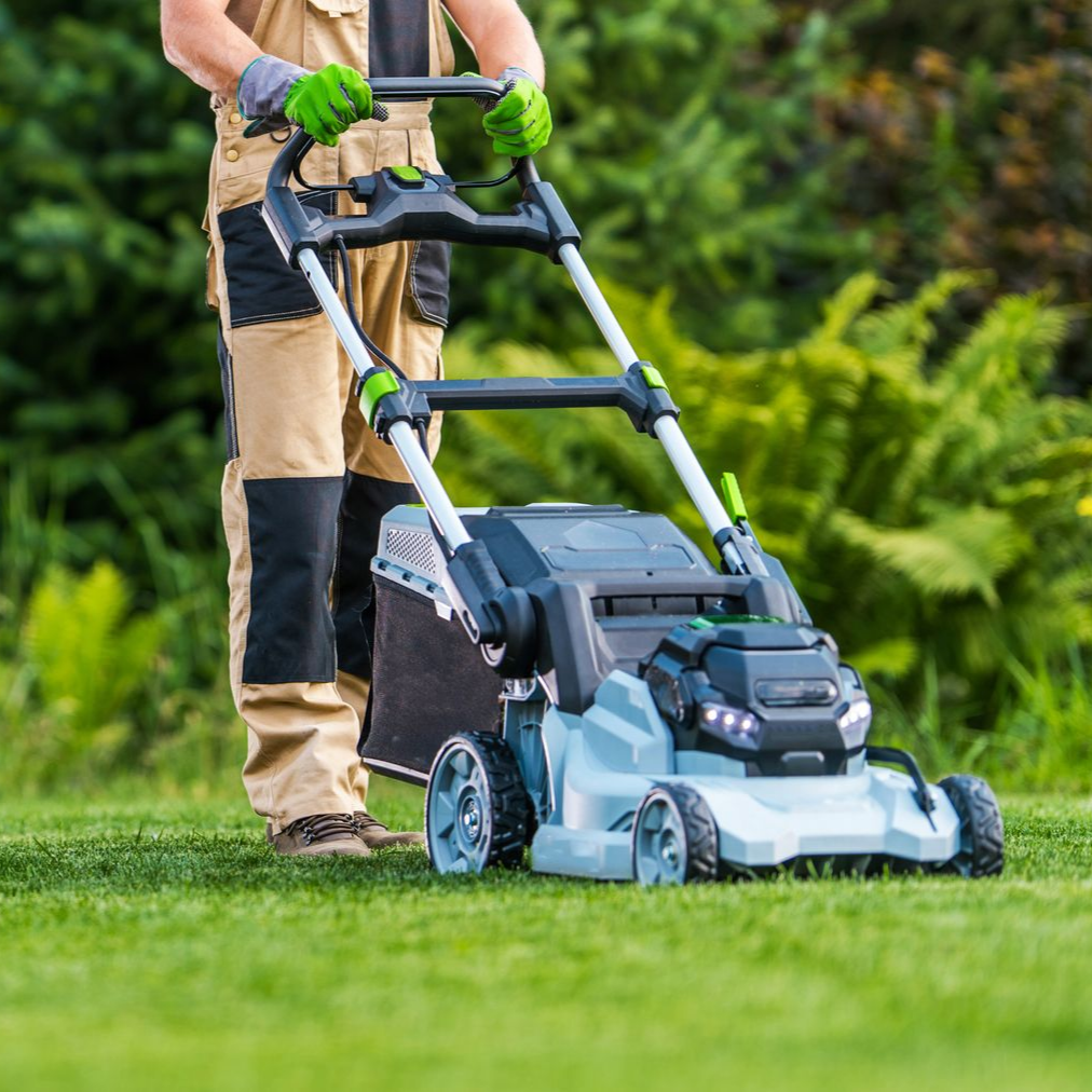 Par une journée ensoleillée, une personne vêtue d'une combinaison de travail beige et noire tond une pelouse d'un vert luxuriant avec une tondeuse électrique bleu clair.