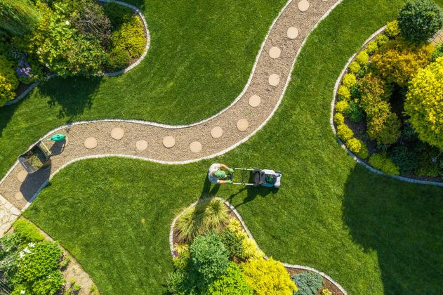 Vue aérienne d'une personne tondant une pelouse à côté d'un chemin de pierre sinueux dans un jardin paysager.