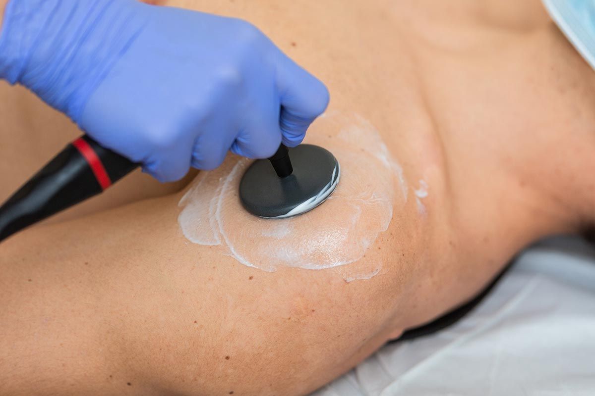 Una persona recibe terapia de ultrasonido en el hombro. Un profesional de la salud sostiene el dispositivo con una mano enguantada azul.