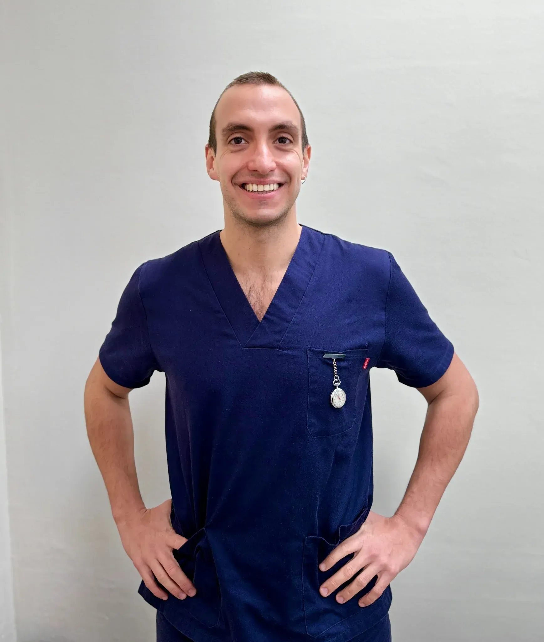 Un hombre con uniforme azul sonríe, con las manos en las caderas, frente a una pared blanca.