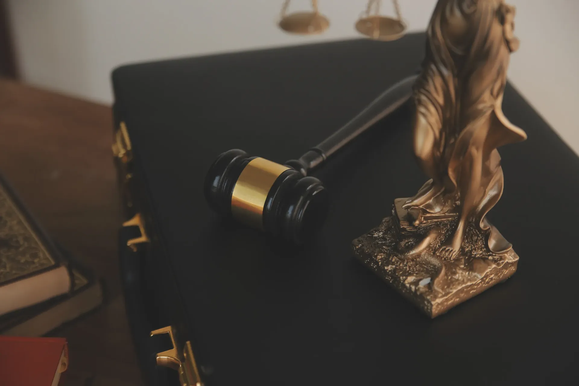 Un libro de leyes y un mazo junto a una estatua de bronce de la Dama de la Justicia sobre una superficie oscura.